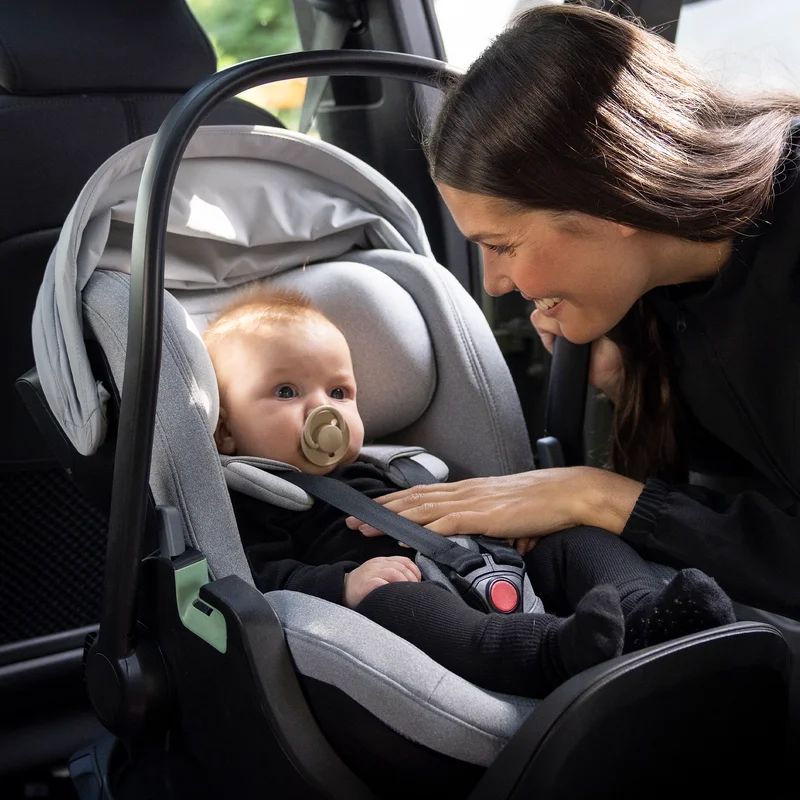 Eine Mutter schaut auf ihr Kleinkind, das in einem Autositz sitzt.