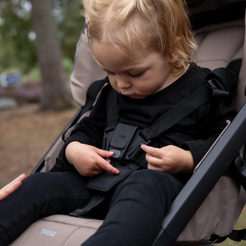 Familie sitzt im Sand neben einem geparkten Thule Urban Glide 4-Rad-Kinderwagen.