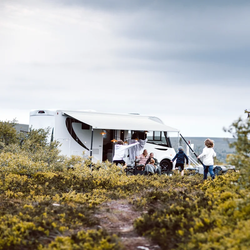 A motorhome is parked in the countryside with a Thule 4200 rv awning with a family running around it.