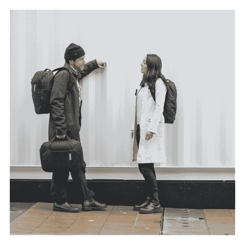 A man and woman stand by a metal structure with a black Thule Accent laptop bag.