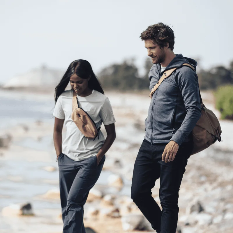 Zwei Personen gehen einen Strand entlang, der Mann trägt eine Sporttasche und die Frau eine Thule Aion Sling Bag.