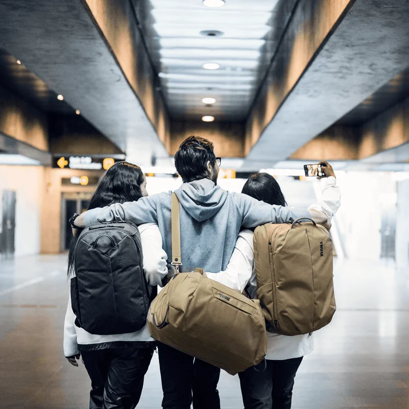 Drei Freunde machen ein Selfie in einer U-Bahn-Station mit Rucksäcken und einer hellbraunen Thule Aion Reisetasche.