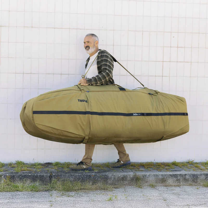 Ein Mann trägt die Thule Aion Surfboardtasche mit einem Riemen über der Schulter.