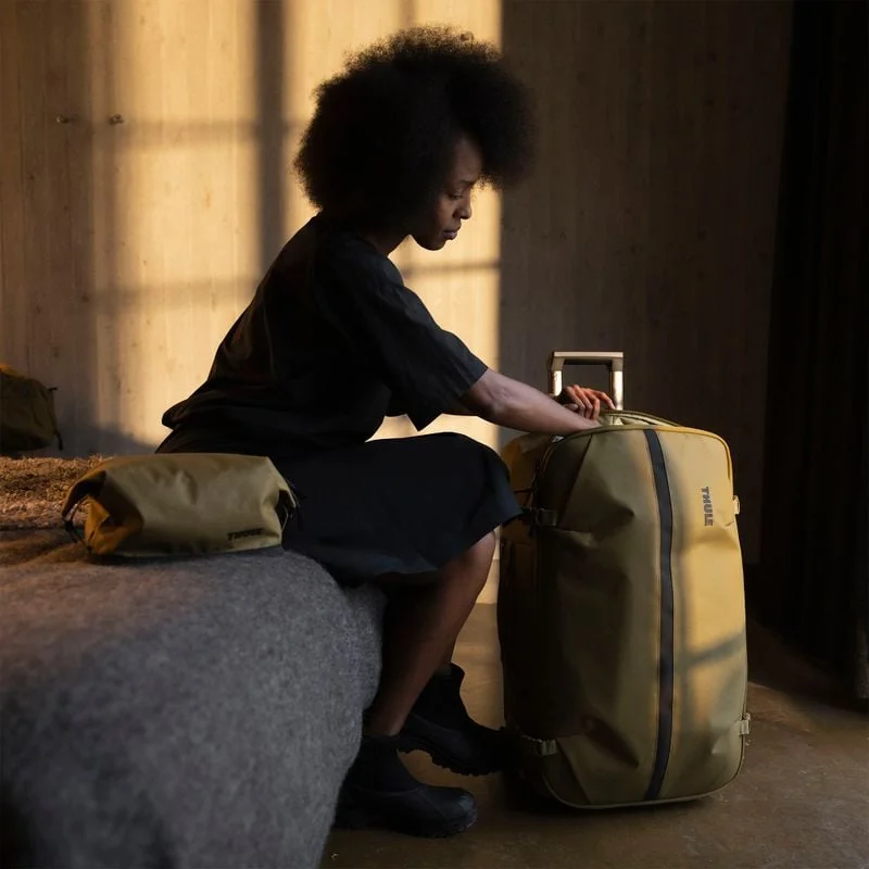 Frau packt einen Thule Aion Rollkoffer und sitzt mit einer passenden Tasche auf einem Bett.