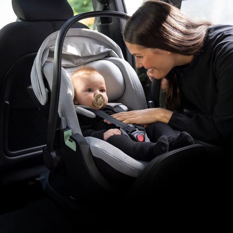 Eine Mutter schaut auf ihr Kleinkind, das in einem Thule Maple Babysitz sitzt, der auf der Thule Alfi Autositzbasis befestigt ist.