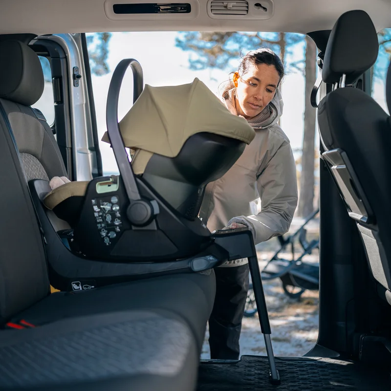 Adult securing a child in a rear-facing car seat attached to the Thule Alfi Connect ISOFIX base inside a vehicle.