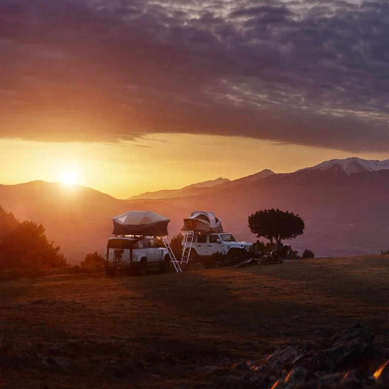 Two cars with roof top tents parked in a hilly terrain in sunset