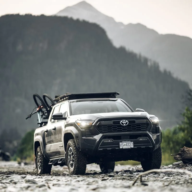 An off-road pickup truck is parked in an outdoors area with a Thule Caprock roof platform and a rail mount on the roof and a Thule ReVert hitch bike rack on the back of the truck with 6 bikes.