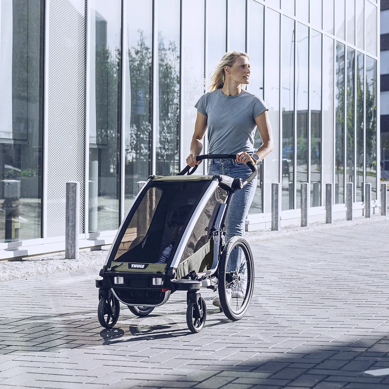 Eine Frau spaziert mit ihrem Thule Chariot Lite Kinderfahrradanhänger durch eine Stadtstraße.