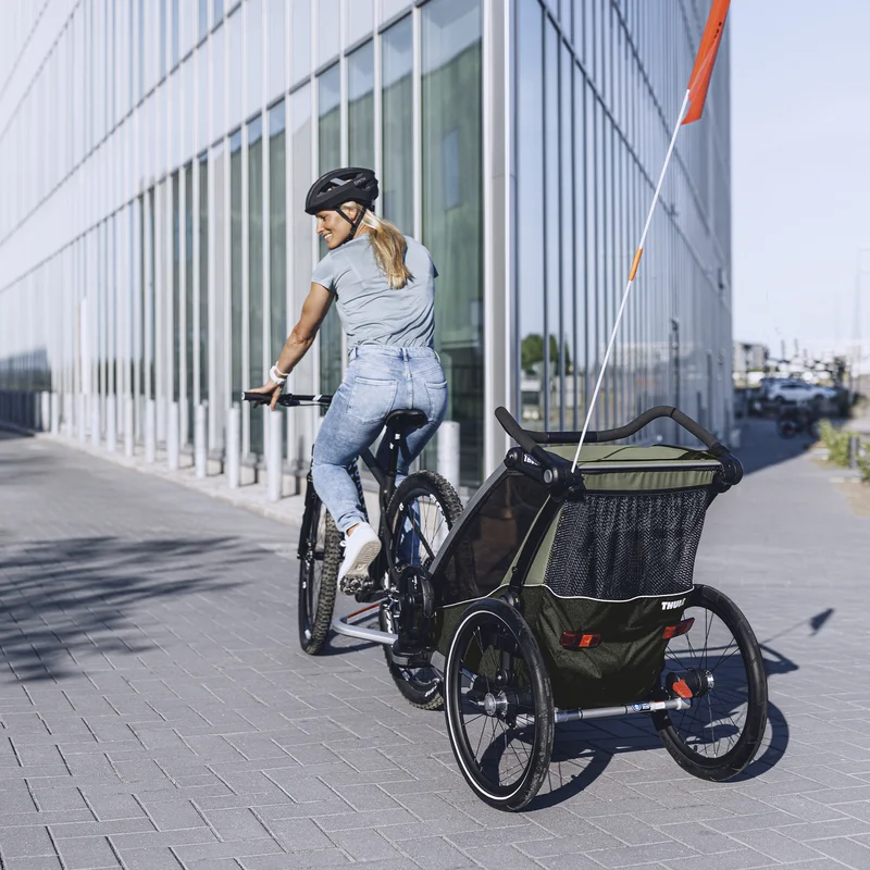 Eine Frau fährt mit ihrem Kind im Thule Chariot Lite Fahrradanhänger die Straße entlang.
