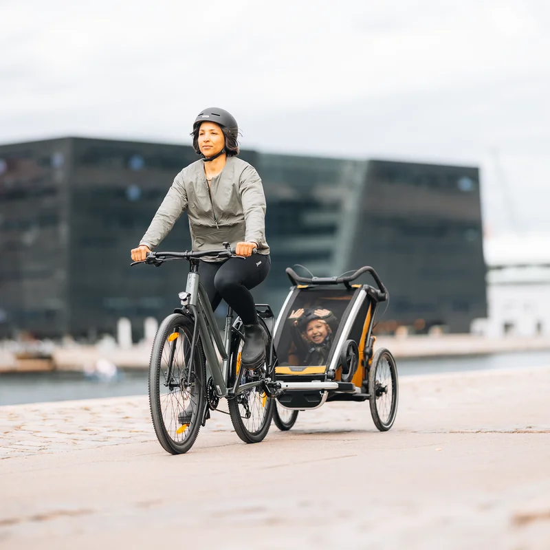 Person, die mit einem Thule Chariot Sport 2 Fahrradanhänger durch die Stadt radelt und aktiven Transport mit alltäglichem Komfort verbindet.