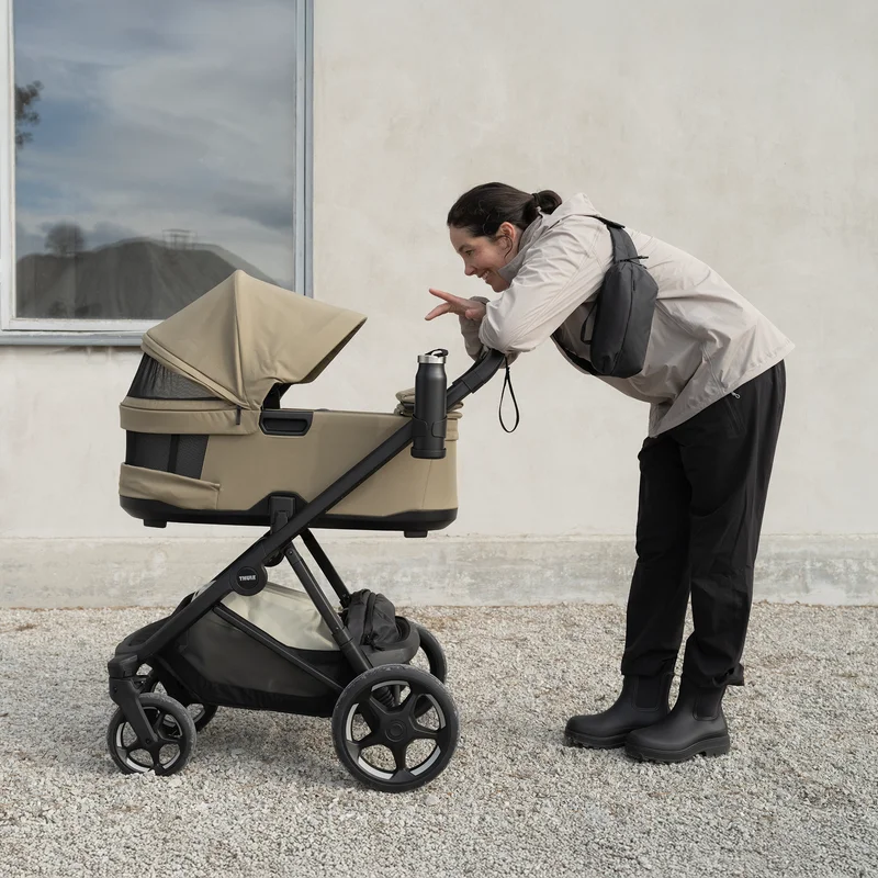 Adult leaning over a Thule Charm stroller outdoors.