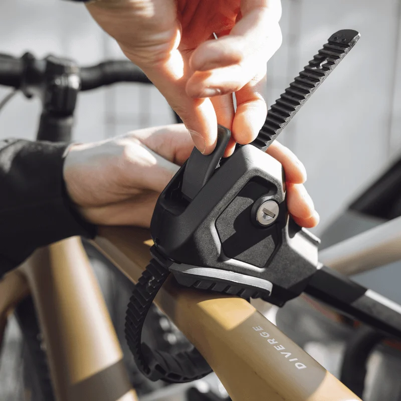 Close-up of a person fastening a bike to a rack using a secure strap mechanism on the frame of the bicycle.