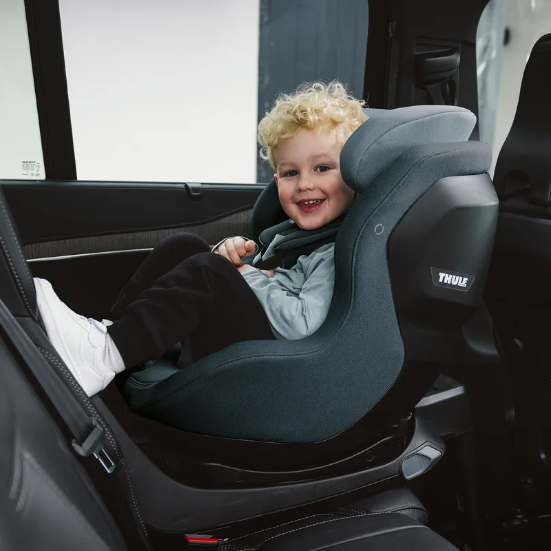 Ein lächelndes Kind, das in einem Thule Elm Kindersitz in einem Fahrzeug sitzt.