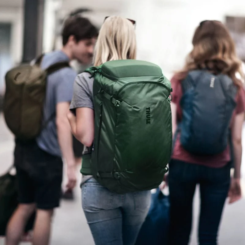 Three friends stand on a train platform carrying Thule Landmark travel backpacks.
