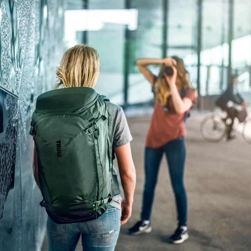 A woman is taking a picture of a friend with a Thule Landmark 40L travel backpack