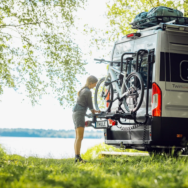 A woman loads a bike onto the Thule VeloTrack, equipped with the Thule Lightboard Van accessory, allowing the bike to be mounted lower on the van for easier loading and improved visibility of taillights.