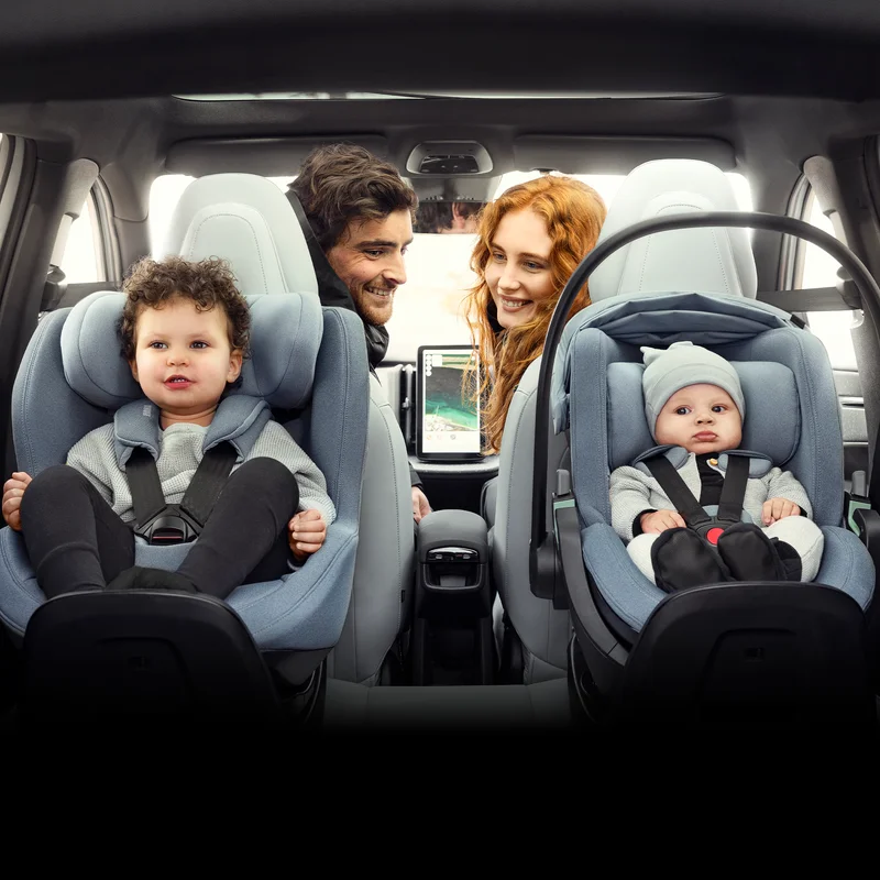 Ein Säugling und ein Kleinkind sitzen in ihren Autositzen im hinteren Teil eines Autos, während ihre Eltern einen Blick auf sie werfen.