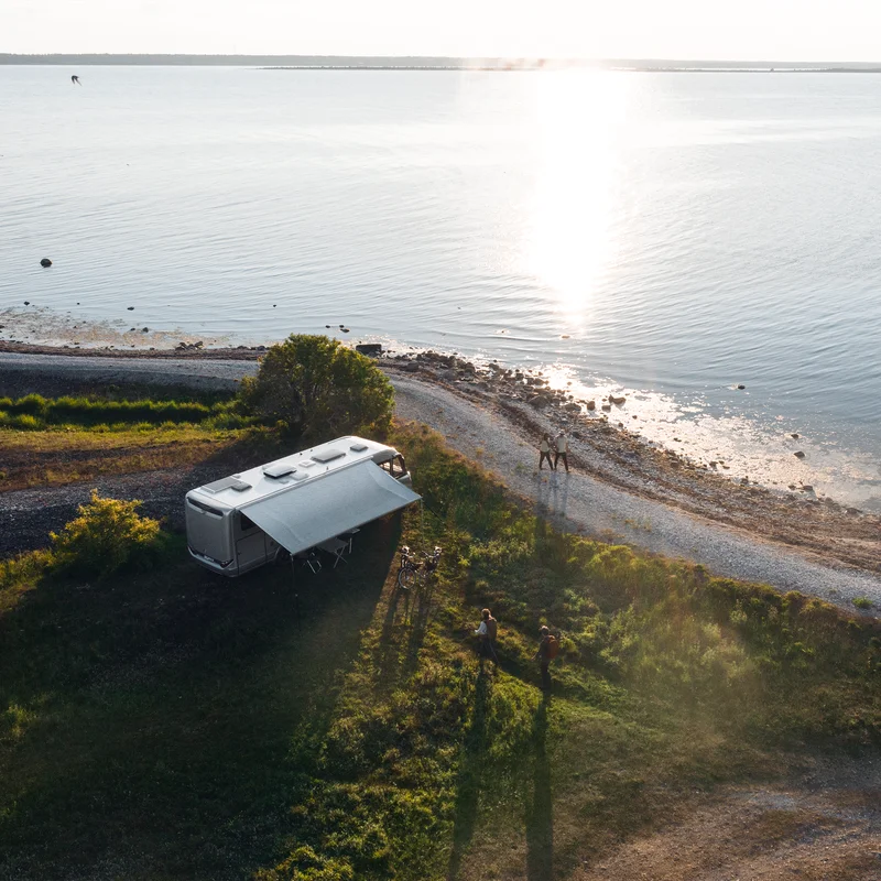 A motorhome is parked next to a lake where the sun is setting and it has a Thule Omnistor 8000 RV awning.
