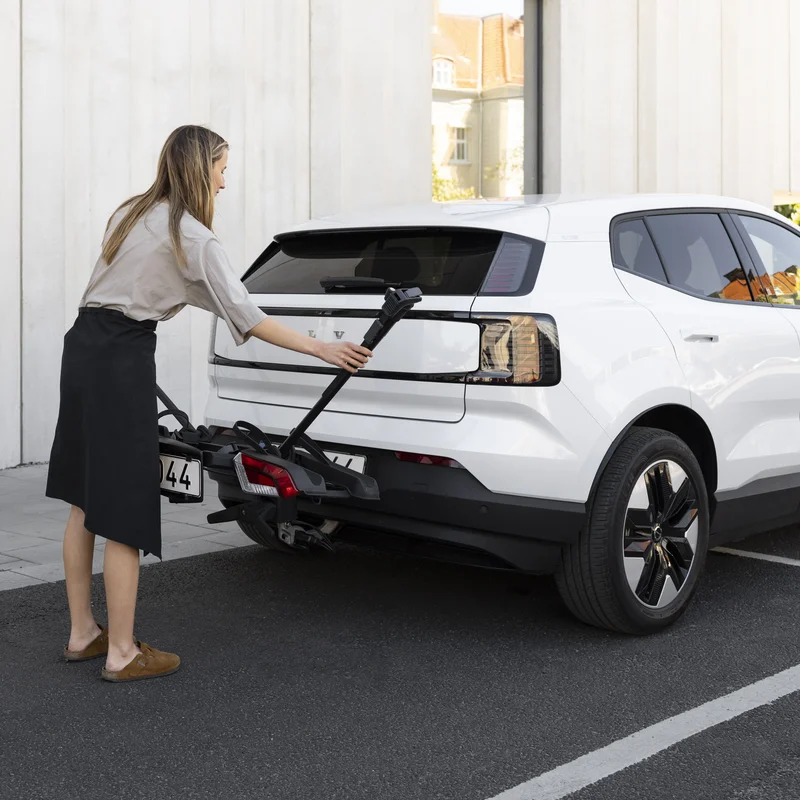 A woman moves a bike arm on a Thule OutPace bike carrier mounted on a white car.