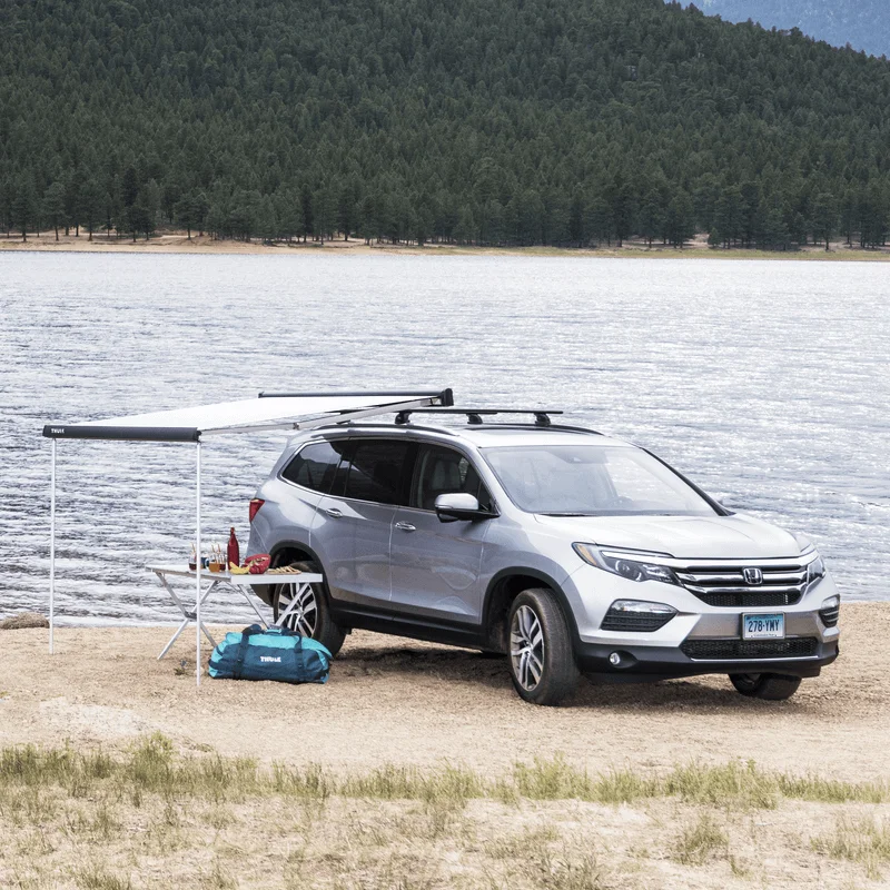 A group of people sitting on a beach close to a car with a Thule Outland Awning