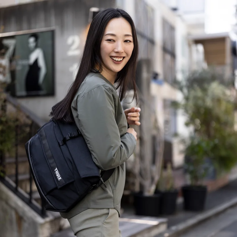 Woman walks down a street with a Thule Paramount 14L messenger bag.
