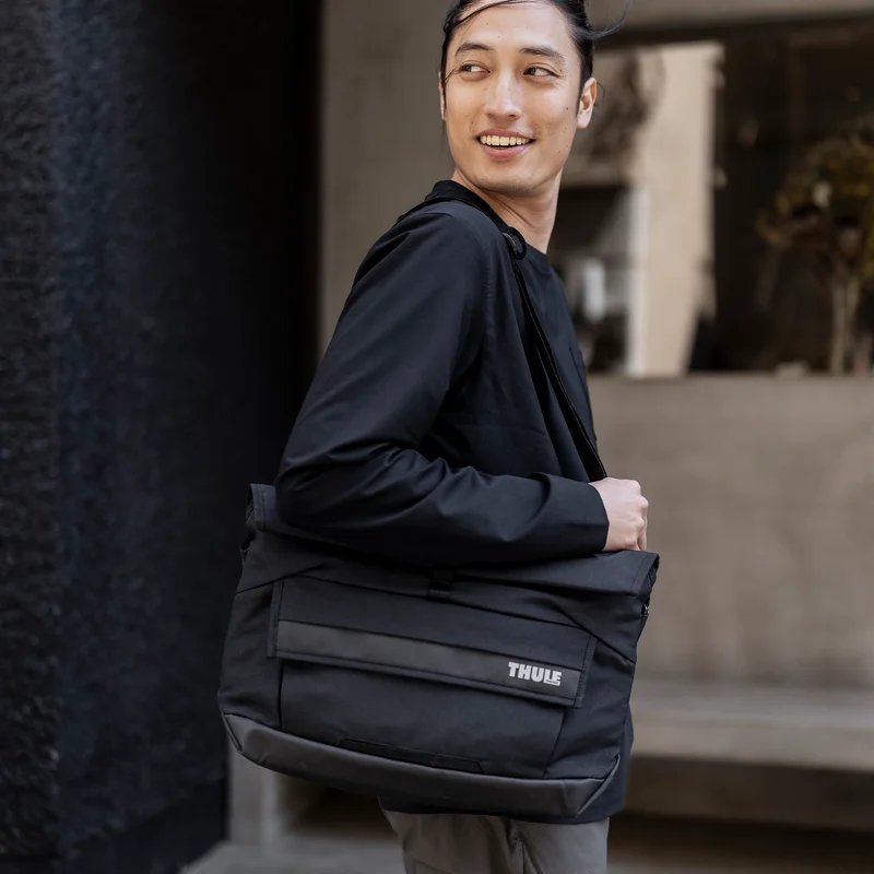 A man stands outside a cafe with a black Thule Paramount 14L messenger bag.