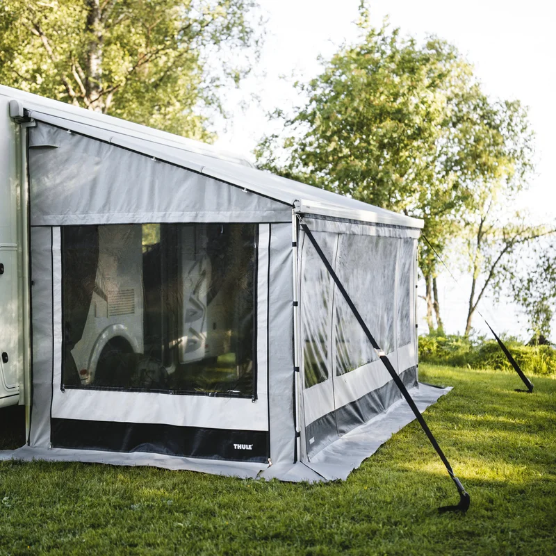 Thule awning with full awning tent set up beside a camper on a grass field near trees