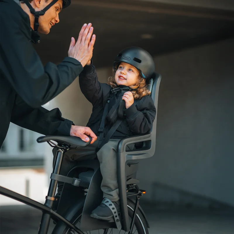 Elternteil gibt einem lächelnden Kind, das im Thule RideAlong 2 Fahrradsitz sitzt, ein High-Five.