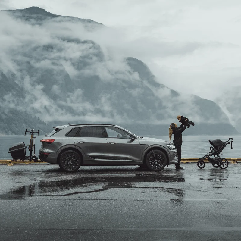 A car is parked by the water next to a family with a Thule Santu towbar cargo carrier
