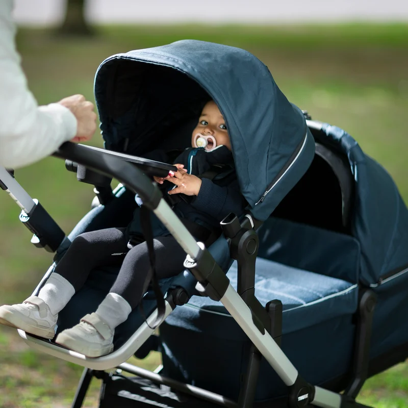 A baby sits in a blue double stroller thanks to the Thule Sleek Adapter Kit.