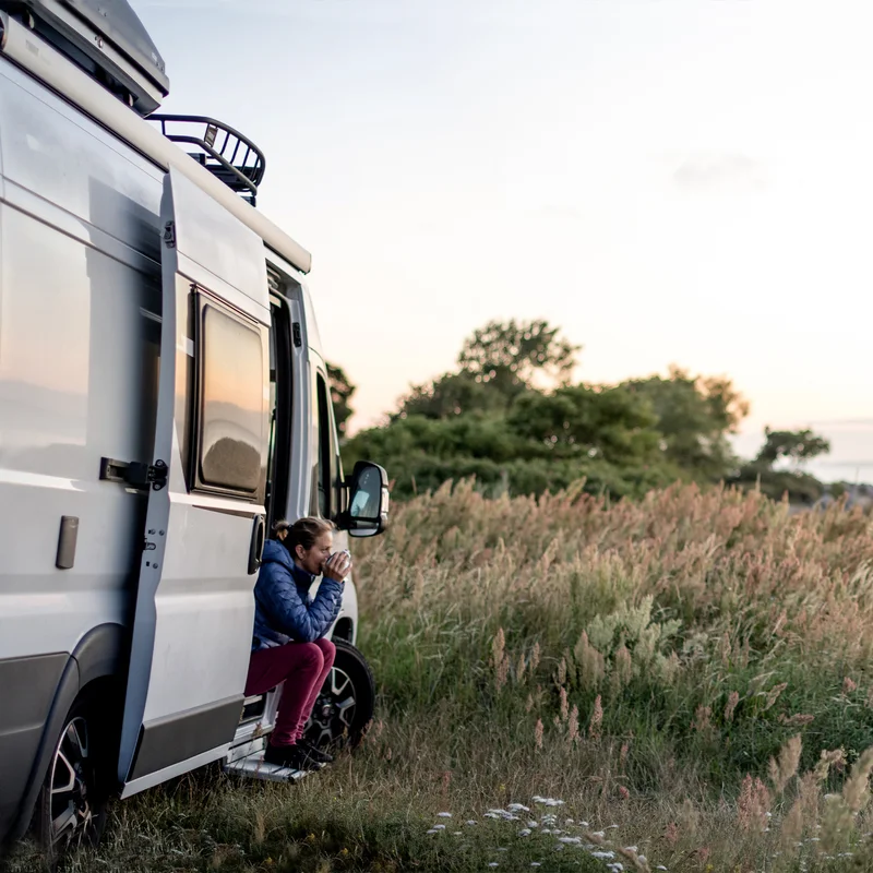 A van is parked in the grass and has a Thule Slide-Out Step van step.