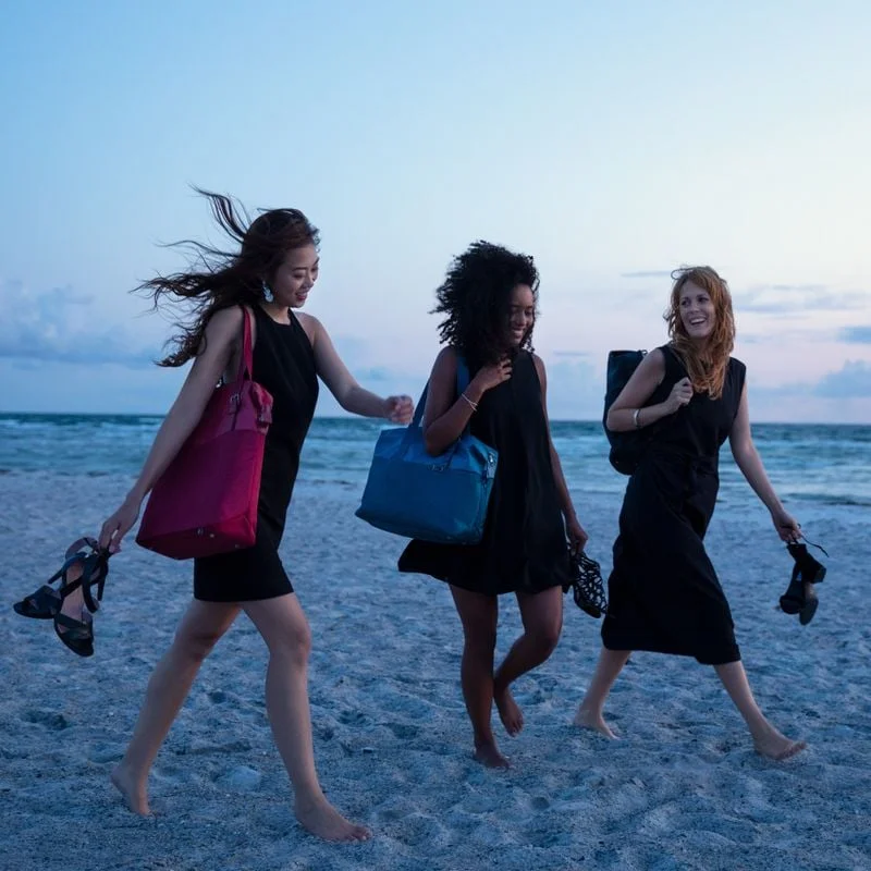 Three women walk on the beach carrying Thule Spira weekender bags.