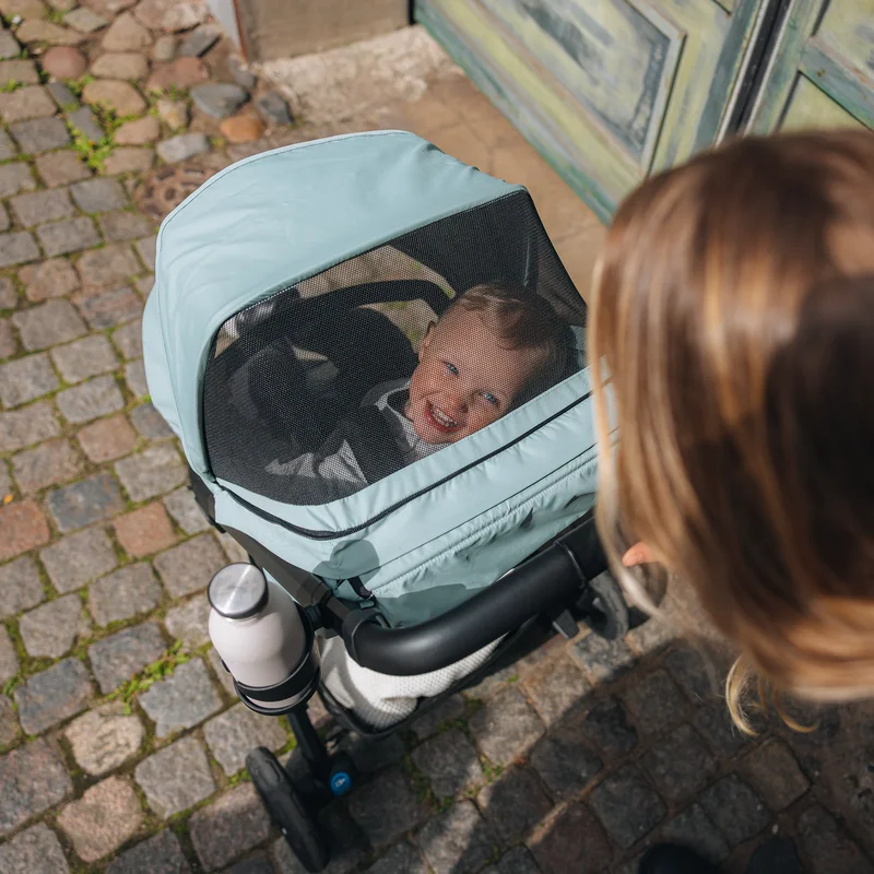 Kind schläft im Thule Spring 2 Kinderbett mit Netzabdeckung, während eine Frau zusieht.