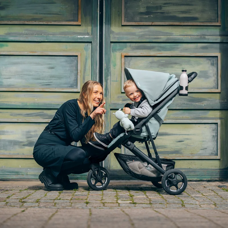 Frau hockt neben Kleinkind im Thule Spring 2 Kinderwagen auf Kopfsteinpflasterstraße.