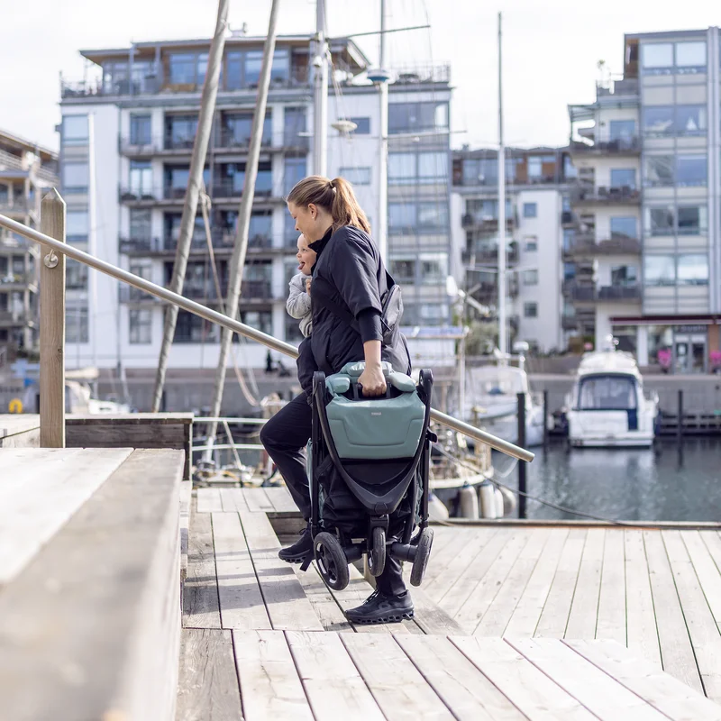 Frau trägt den zusammengeklappten Thule Spring 2 Kinderwagen am Hafen.