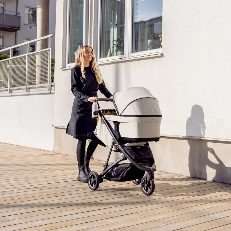 Frau schiebt Thule Spring 2 mit Kinderwagen auf sonniger Straße.