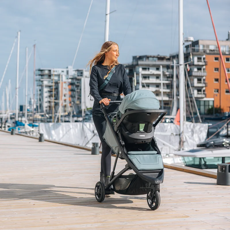 Frau schiebt Thule Spring 2 mit Bassinet am Hafen entlang.