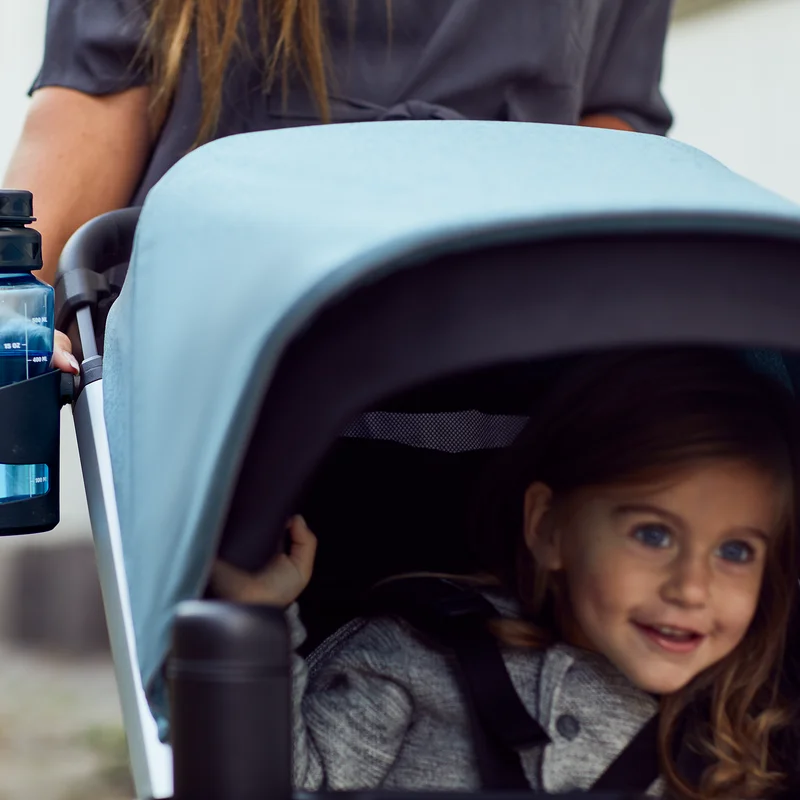 A toddler sits in a stroller with a blue Thule Spring Canopy.