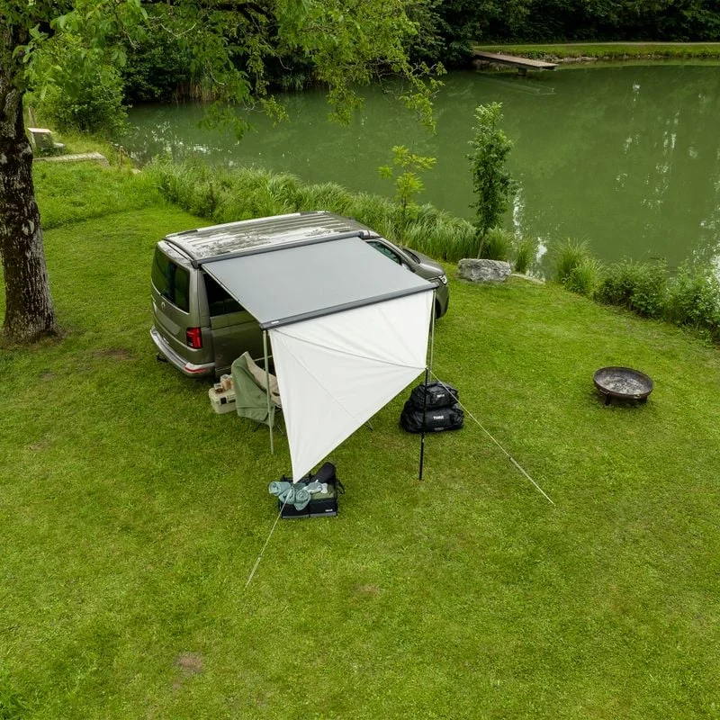 A van is parked next to the water with the Thule Subsola versatile awning panels.