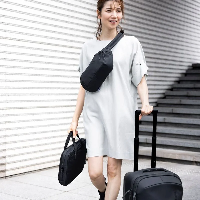 A woman walks down stairs with a black Thule Subterra suitcase, sling and briefcase.