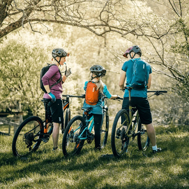 Three cyclist stand in the forest on their bikes with Thule Uptake hydrations packs.