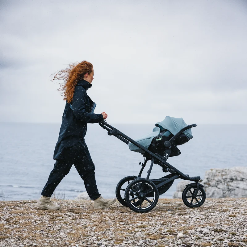 Frau geht mit dem Thule Urban Glide 3 Kinderwagen vor einer Holzwand spazieren.