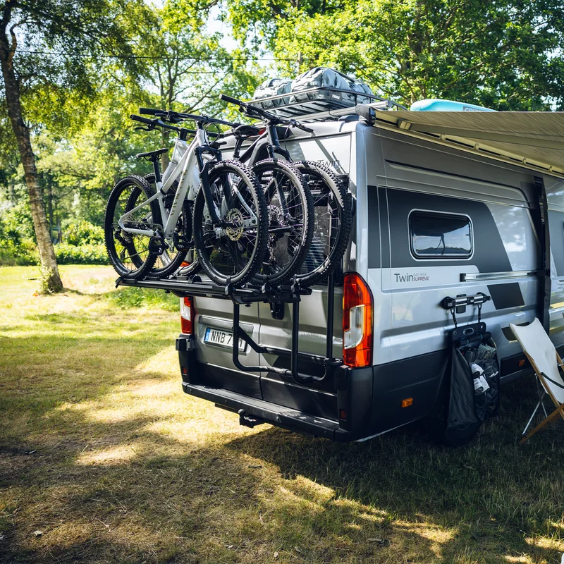 A camper van equipped with the Thule VeloTrack 3rd Rail Kit, securely holding three bikes at the rear. The sturdy setup allows for expanded bike transport while maintaining easy access to the van.