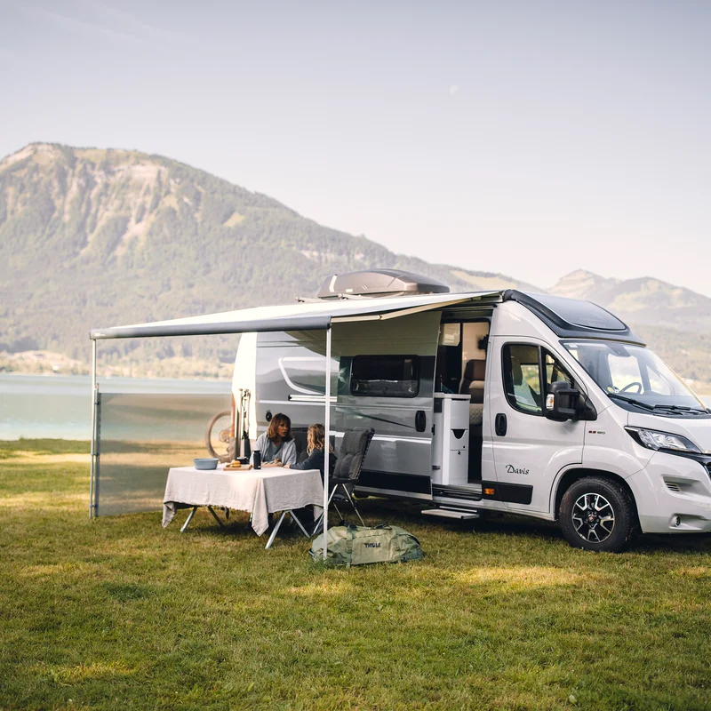 An rv parked next to a lake and a mountain with an awning and a Thule View Blocker Side awning side wall.