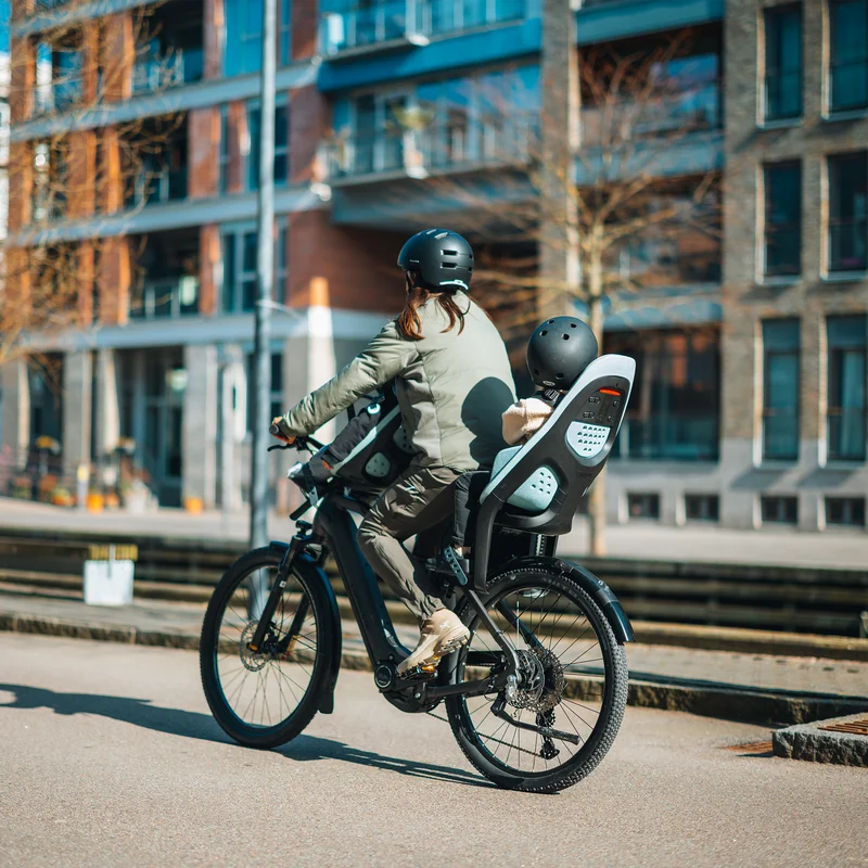Eine dynamische urbane Radszene mit einem Elternteil und einem Kind, wobei das Kind sicher in einem Thule Yepp 2 Fahrradkindersitz hinten sitzt.