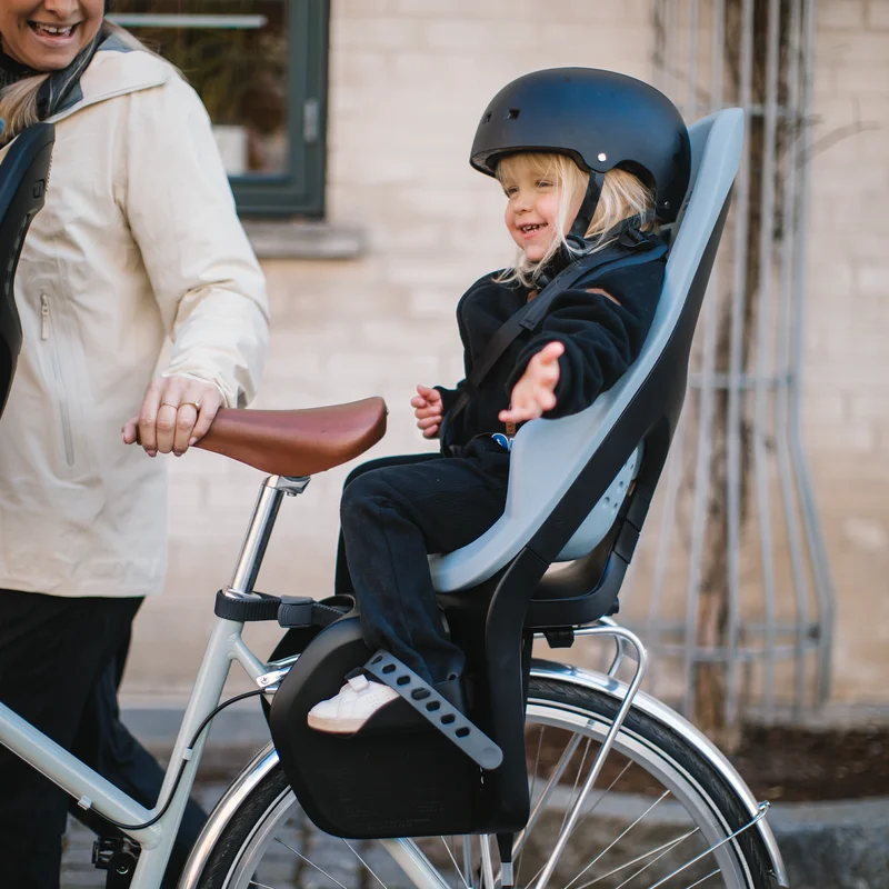 Ein lächelndes Kind sitzt in einem blauen Yepp 2 Maxi Kindersitz für Fahrräder.