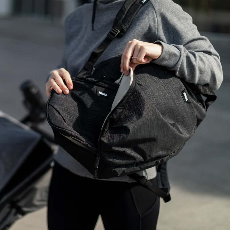 A woman unzips her black Thule Changing Backpack and takes out another bag inside.