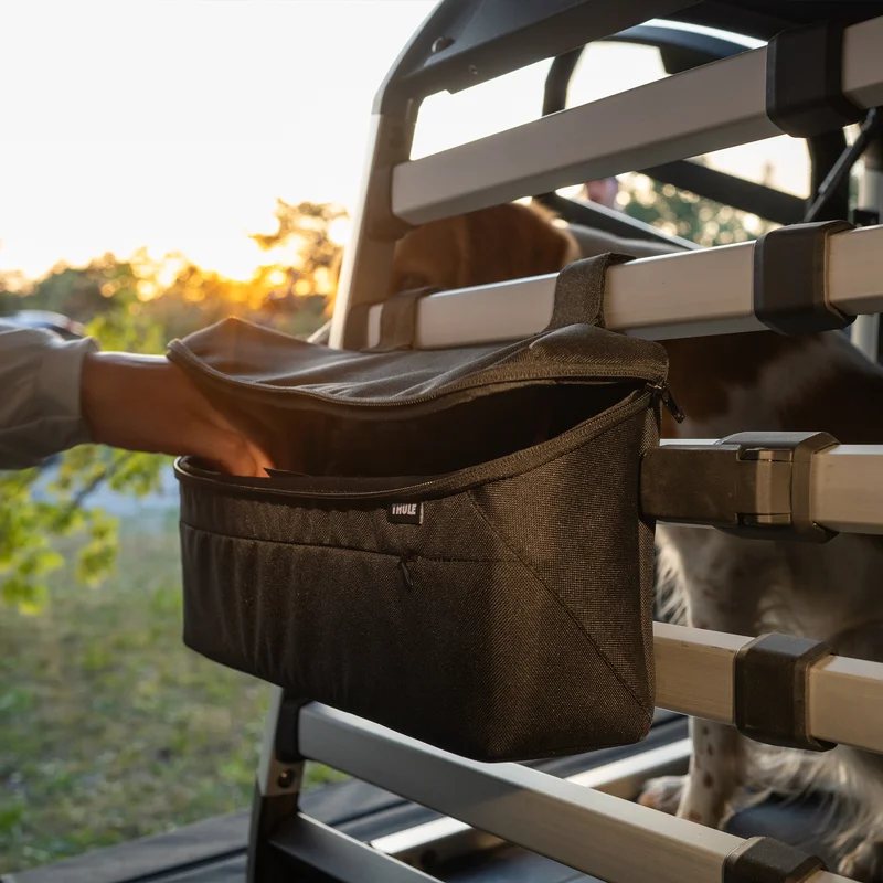 Someone reaches for the Thule Dog crate storage bag attached to the Thule Allax dog crate for cars.