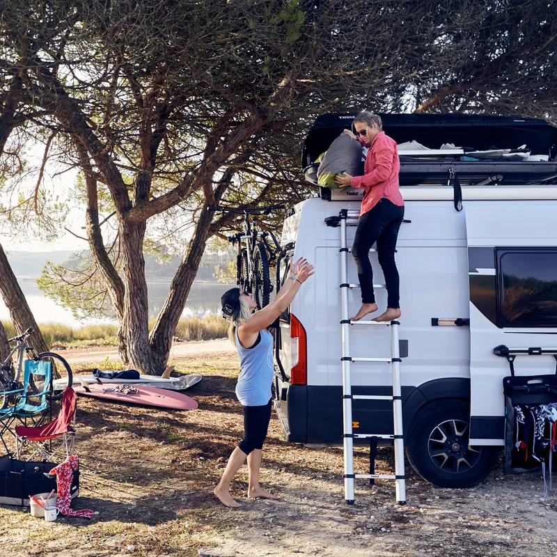 A van is parked near a lake with a Thule Van Ladder 9 Steps van ladder.